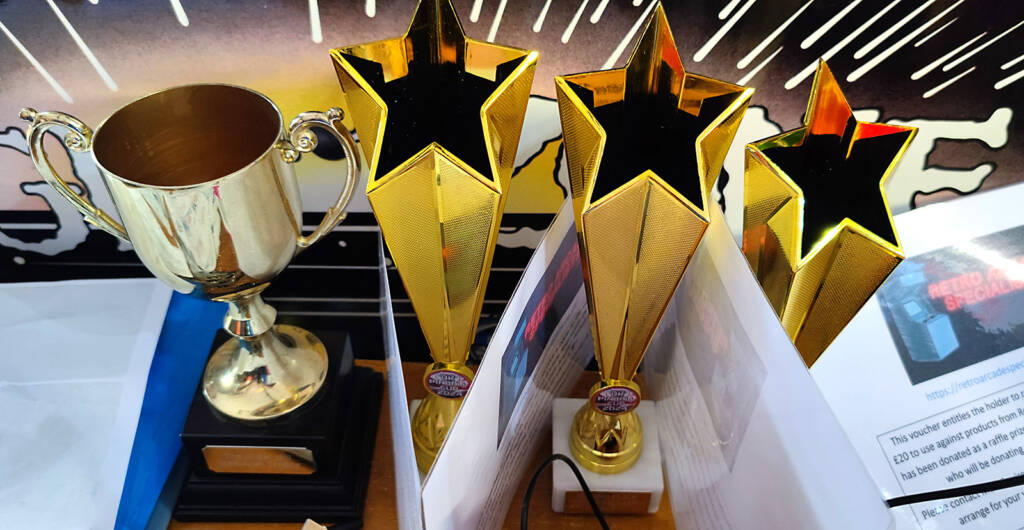 Trophies and prizes for the UK Pinball Cup alongside the Nigel Hill Memorial Trophy, commemorating a much-missed UK pinball stalwart