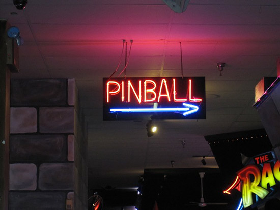A large neon sign pointing the way to the pinball machine room